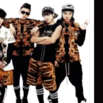 Imagem do BTS na era "2 COOL 4 SKOOL", com os membros vestindo roupas douradas e pretas de estilo hip-hop. Ao lado, o título da música "Like BTS", presente no álbum de estreia, representando a capa do artigo com a letra da canção no site Bangtan Now.