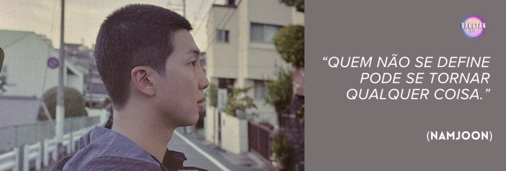 Imagem do Bangtan Now com RM (Namjoon), do BTS, de perfil, parado em uma rua residencial tranquila, cercada por casas e postes de energia, sob a luz suave do início da manhã ou fim da tarde. Ele veste um moletom escuro e olha contemplativo para a distância. No lado direito da imagem, sobre um fundo em tom malva apagado, há uma citação em texto branco: “Quem não se define pode se tornar qualquer coisa.” (Namjoon). O logo do Bangtan Now aparece no canto superior direito, conectando a frase aos temas de identidade e introspecção explorados no documentário RM: Right People Wrong Person.