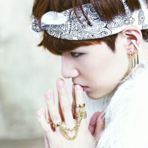 SUGA no conceito marcante do bts o rul82 album, exibindo detalhes como acessórios dourados e a icônica bandana, que reforçam o estilo ousado da era. Descubra mais sobre essa fase no Bangtan Now.
