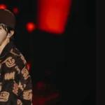 Imagem de capa do artigo sobre LV Bag, colaboração de Don Toliver, Pharrell Williams e J-Hope. A imagem apresenta J-Hope no palco, vestindo um look estiloso e com iluminação avermelhada ao fundo. No lado direito, o título destaca a parceria, junto com o logotipo do Bangtan Now.