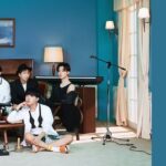 Imagem do BTS em um ambiente acolhedor com decoração clássica e tons azulados, remetendo à estética do álbum BE. Os sete membros estão dispostos de maneira descontraída na sala, cercados por instrumentos musicais como teclado, guitarra e percussão. Jungkook segura uma guitarra, enquanto Suga está sentado no chão com um tamborim próximo. RM usa um chapéu e J-Hope veste roupas confortáveis, refletindo a atmosfera intimista do conceito do BE. Essa imagem faz parte do artigo sobre os agradecimentos do álbum BE, onde os membros expressam suas emoções e gratidão pelo ARMY durante um período desafiador. Imagem que ilustra o artigo do Bangtan Now.