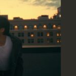Imagem de capa do artigo do portal Bangtan Now sobre a BTS Angel Anniversary Edition. A imagem mostra Jimin em uma cena do pôr do sol, em um terraço urbano, vestindo jaqueta de couro e camiseta branca, cantando com expressão emotiva. Ao lado direito, sobre fundo escuro, aparecem os textos "ARTIGOS", "COLLABS • JIMIN" e o título "BTS ANGEL ANNIVERSARY EDITION".