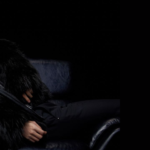 Imagem de capa do artigo do Bangtan Now sobre o álbum Echo do Jin. Jin aparece reclinado em uma poltrona preta, usando um casaco de pelúcia escura, com expressão contemplativa em um fundo totalmente preto. Ao lado, está escrito: "Álbum Echo do Jin – emoção, vocais impecáveis e um presente para o ARMY", com o logo do Bangtan Now no canto superior. A imagem transmite a atmosfera sofisticada e emocional do conteúdo.