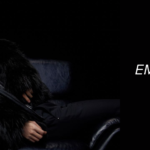 Jin reclines on a dark leather chair wearing a luxurious black fur coat, set against a black background. The right side of the image features bold white text that reads "Jin's Echo album: Emotion, flawless vocals, and a gift for ARMY," along with the Bangtan Now logo. This promotional banner highlights the emotional depth and vocal brilliance of Jin's Echo album, inviting fans to explore more on Bangtan Now.