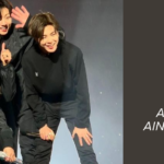 Imagem do grupo BTS durante um show no Brasil, com todos os sete integrantes sorrindo e interagindo carinhosamente no palco, vestidos de preto. Ao fundo, luzes suaves realçam a emoção do momento. À direita, há um fundo escuro com os dizeres: “BTS Brasil – Histórias de um relacionamento antigo e intenso, que ainda vai render muito!”, destacando o título do artigo publicado no site Bangtan Now. Esta imagem ilustra a forte conexão entre o BTS e o público brasileiro, tema central do conteúdo especial sobre BTS Brasil no Bangtan Now.