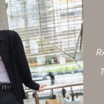 Jin, member of BTS, is leaning against a railing inside a modern building with large glass windows, wearing a black open shirt over a gray printed tank top and a studded belt. This image is from the official Photo Sketch of Don't Say You Love Me, published on Weverse. On the right side, against a beige background, there's text that reads: "Don't Say You Love Me — Raw emotion in Jin's new song that touched the heart of ARMY," alongside the Bangtan Now logo. The photo captures the elegant style and emotional tone of the release.