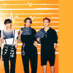 Cover image for the article “BTS Butter: Lyrics and All the Details Behind the Hit” on Bangtan Now. The photo features all seven BTS members standing side by side in front of an orange wall with a heartbeat line design. Each member is wearing a black outfit and holding a police-style placard with numbers. From left to right: the first member holds a sign reading “000001”; the second’s reads “660660”; the third, “201904”; the fourth, “655212”; the fifth, “384627”; the sixth, “110604”; and the seventh, “141018”. On the right side of the image, set on a solid orange background, the text reads: “BTS BUTTER – Lyrics and All the Details Behind the Hit” along with the Bangtan Now logo.
