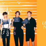 Imagen de portada del artículo “BTS Butter: Letra, traducción y todos los detalles detrás del éxito” en Bangtan Now. La foto muestra a los siete miembros de BTS de pie, uno al lado del otro, frente a una pared naranja con un diseño de línea de ritmo cardíaco. Cada uno viste ropa negra y sostiene una placa de estilo policial con números. De izquierda a derecha: el primer miembro sostiene un cartel con el número “000001”; el segundo, “660660”; el tercero, “201904”; el cuarto, “655212”; el quinto, “384627”; el sexto, “110604”; y el séptimo, “141018”. A la derecha de la imagen, sobre un fondo naranja sólido, aparece el texto: “BTS BUTTER – Letra, traducción y todos los detalles detrás del éxito”, junto al logotipo de Bangtan Now.