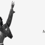 Imagen promocional en blanco y negro de Jungkook Calvin Klein. Jungkook aparece de pie, en el centro, con los brazos levantados en señal de confianza. Lleva una chaqueta de mezclilla abierta que deja al descubierto su torso definido y parte del calzoncillo con el logo de Calvin Klein visible. Su expresión es seria y poderosa, con el cabello oscuro cayendo sobre los ojos. A la derecha de la imagen, sobre fondo blanco, se lee el título del artículo: “Jungkook Calvin Klein: La alianza que conquistó el mundo de la moda”, junto al logo del blog Bangtan Now. La imagen transmite fuerza, estilo y modernidad, reforzando la identidad visual de la campaña de Jungkook como embajador de la marca Calvin Klein.