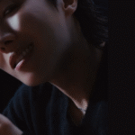 Cover image for the article “SPAGHETTI j-hope lyrics – Translation and meaning of the collab with LE SSERAFIM” on the Bangtan Now blog. The scene features j-hope, member of BTS, in a dark and minimalist setting, with soft lighting highlighting his face. He’s holding a metal plate and lifting a fork full of spaghetti, smiling slightly at the camera. The shot is tight, focusing on his expression and the movement of the noodles, capturing the sensual and provocative tone of the SPAGHETTI MV. On the right, against a black background, are the texts “SPAGHETTI J-HOPE LYRICS – TRANSLATION AND MEANING OF THE COLLAB WITH LE SSERAFIM” and the colorful Bangtan Now logo in the upper corner.