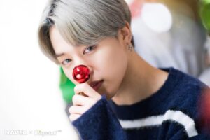 Jimin aparece com uma pequena bola vermelha posicionada no nariz como uma rena glamourosa que trocou trenó por palco, encarando a câmera com aquele olhar hipnotizante que diz "eu sei que você surtou". O suéter azul escuro com listras brancas traz aconchego ao visual, equilibrando o toque de humor com o charme clássico de final de ano. Tudo isso faz parte do especial de Natal do BTS para o Naver, apresentado no artigo do Bangtan Now. BTS Natal nunca foi tão visualmente impactante.