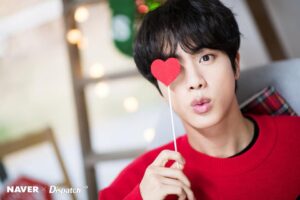 Jin prova que o verdadeiro espírito do BTS Natal vem com um toque de charme e uma boa dose de carisma, posando com um coração vermelho cobrindo um dos olhos e uma expressão de surpresa digna de emoji. Vestindo um suéter vermelho clássico que combina com o acessório, ele transforma um simples momento em puro fanservice natalino. Tudo parte do ensaio especial de fim de ano para o Naver, apresentado no artigo do Bangtan Now — onde até o amor entra como decoração temática.