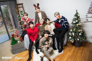 O BTS aparece reunido em um cenário natalino aconchegante, rodeado por decoração festiva, incluindo uma árvore de Natal iluminada, adereços divertidos e um pequeno cachorrinho nos braços de Taehyung, transmitindo uma atmosfera calorosa e familiar. Com roupas confortáveis e sorrisos espontâneos, os integrantes demonstram seu espírito alegre e descontraído, celebrando juntos o fim de ano. A imagem, cheia de cores típicas do Natal como vermelho, verde e dourado, transmite carinho e união entre os membros, sendo parte especial do conteúdo exclusivo do Naver em parceria com a Dispatch. BTS Natal no artigo do Bangtan Now.
