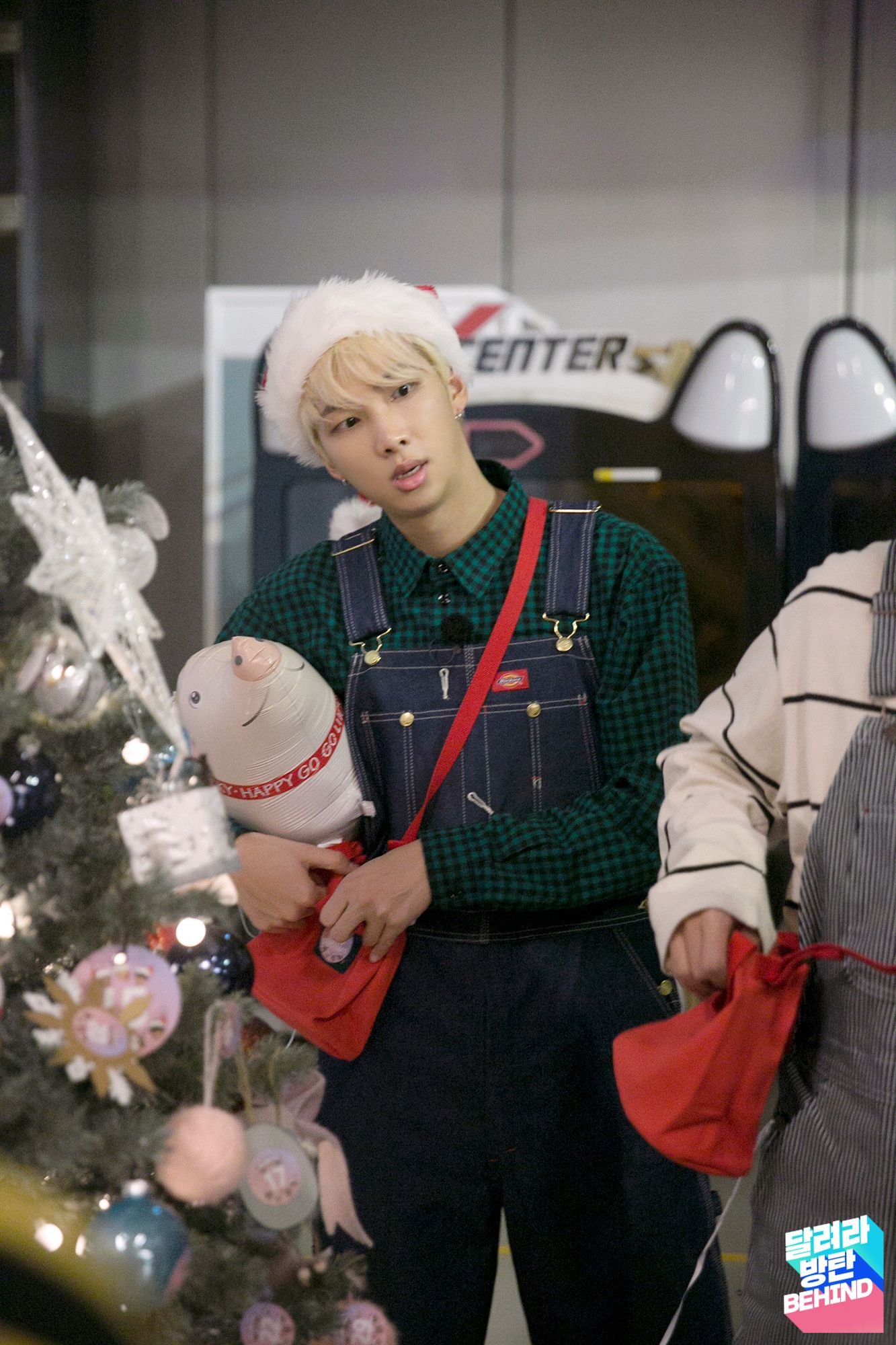 RM in a plaid shirt, denim overalls and Santa hat holding an inflatable pig, Run BTS! Ep. 32