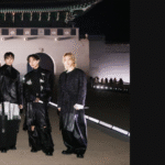 BTS Netflix: cover artwork for the Bangtan Now article, composed of two elements. On the left, an official photo released by Netflix showing all seven BTS members - RM, Jin, SUGA, j-hope, Jimin, V, and Jungkook - posing at night in front of the illuminated gates of Gyeongbokgung Palace at Gwanghwamun Square, Seoul, wearing dark outfits with reinterpreted armor and hanbok elements designed by SONGZIO for BTS THE COMEBACK LIVE | ARIRANG. On the right, a black background featuring the Bangtan Now logo, the "Articles" tag, and the article title: "BTS Netflix Live - Why the Gwanghwamun comeback show is already part of history."