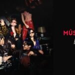 Capa do artigo "Música NORMAL do BTS letra, tradução, pronúncia e significado", categoria Artigos, com o logo do blog Bangtan Now. Foto em tom escuro e clima de festa vintage: os sete membros do BTS posam em roupas coloridas e chamativas, entre estampa de oncinha, paetês e uma pessoa em vestido longo vermelho em pé sobre um sofá, com gestos descontraídos como acenar e se apoiar uns nos outros, ao redor de uma mesa com um bolo.