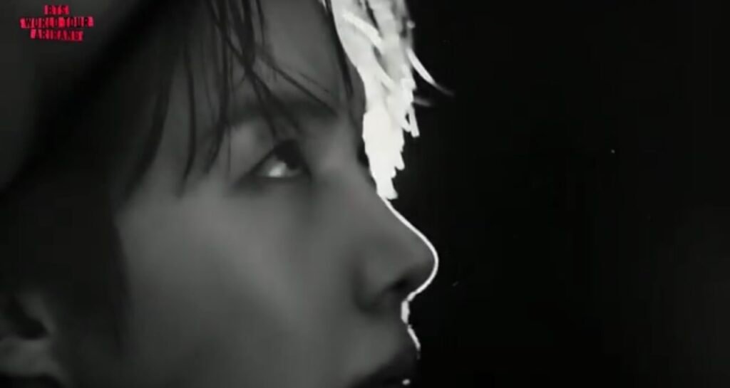 Perfil do rosto de j-hope em preto e branco, cabelo com mecha clara na franja, olhando para cima e para o lado, fundo totalmente escuro, com o logo "BTS WORLD TOUR ARIRANG" no canto superior esquerdo, no VCR dos sete elementos da turnê.
