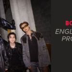 The seven members of BTS pose together backstage at a concert in Chicago, in an industrial concrete hallway with exposed pipes on the ceiling and equipment cases to the left, under a sign reading "Visitor's Locker Room". Six stand side by side in black and gray leather and denim looks, with chains and dark sunglasses. The seventh sits up high on a structure in the center, wearing a white coat and white sunglasses, one leg extended and black knee-high boots. Cover image of the article about Body to Body BTS lyrics, with English translation, pronunciation and the meaning of the song that opens the Arirang album.