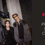 Los siete integrantes de BTS posan juntos entre bastidores de un concierto en Chicago, en un pasillo industrial de concreto con tuberías a la vista en el techo y cajas de equipo a la izquierda, bajo un letrero que indica "Visitor's Locker Room". Seis están de pie uno al lado del otro, con looks negros y grises de cuero y jeans, con cadenas y lentes oscuros. El séptimo aparece en lo alto, sentado sobre una estructura al centro, con abrigo y lentes blancos, una pierna estendida y botas negras de caña alta. Imagen de portada del artículo sobre Body to Body BTS letra, con traducción, pronunciación y significado de la canción que abre el álbum Arirang.